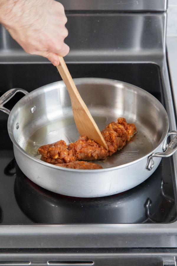 Breaking up half a pound of spicy italian chicken sausage in a stainless steel saucepan.