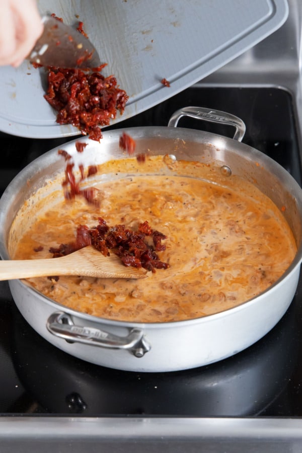 Adding chopped sundried tomatoes to saucepan along with creamy tomato sauce.