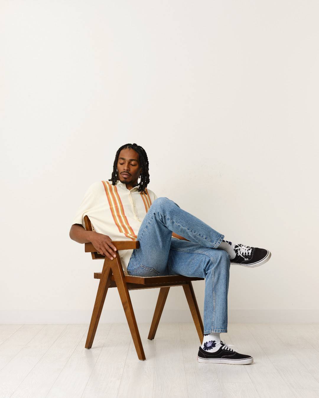 man sitting on a chair wearing a short sleeved polo shirt and jeans