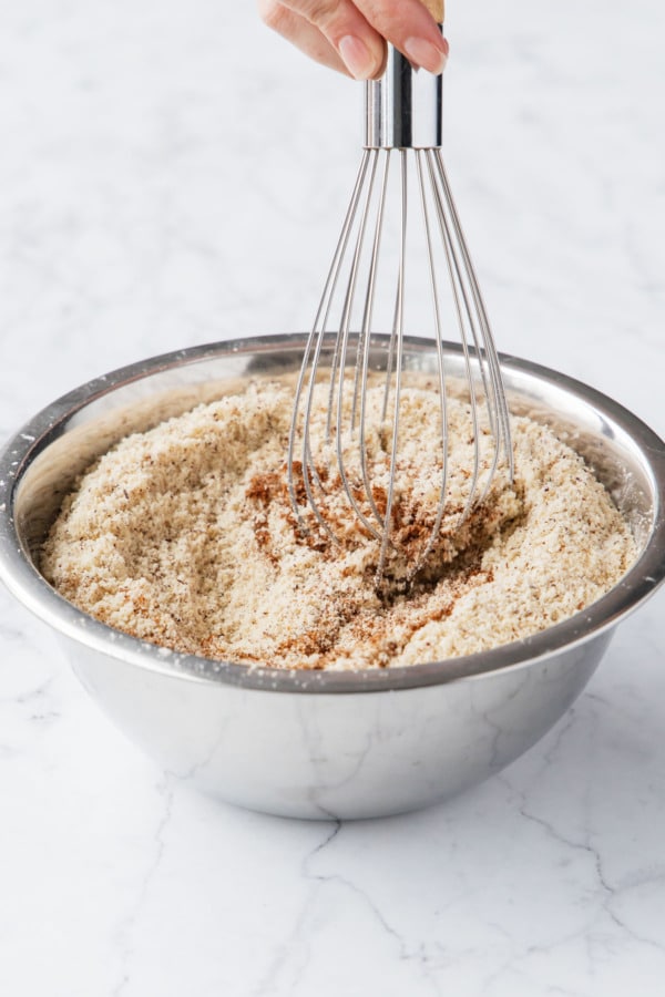 Whisking hazelnut flour with cornstarch, salt, and espresso powder in a small metal mixing bowl.