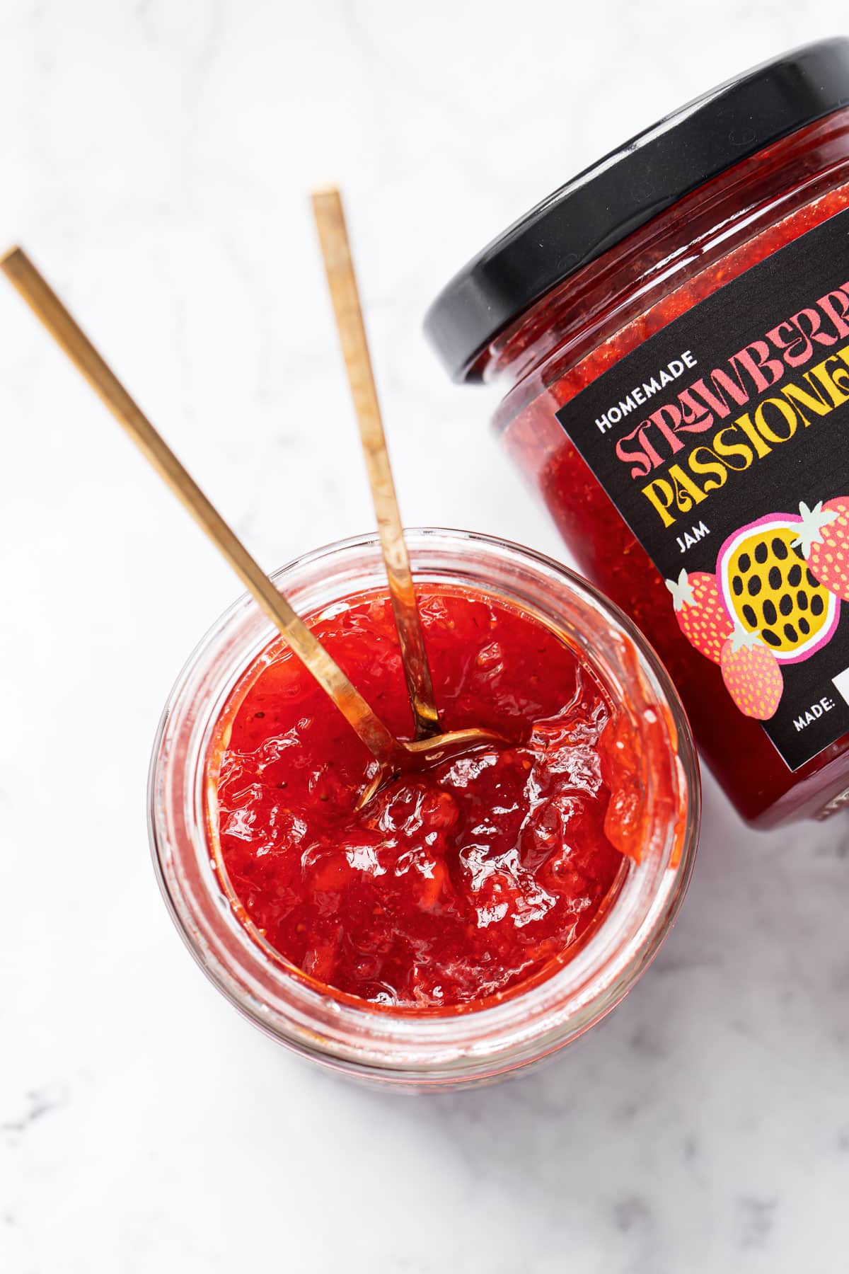 Overhead, looking down into a jar of homemade Strawberry Passionfruit Jam, with a second jar on its side to show the printable label design.