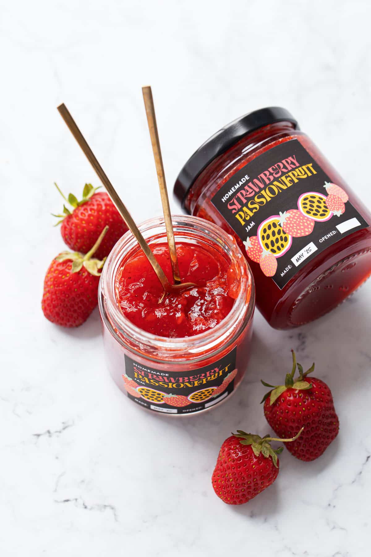 Two jars of Strawberry Passionfruit Jam, one open to show the jam consistency and the other on its side to show the designed label.