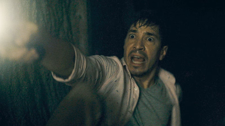 AJ, looking frightened, holds out a flashlight in a dark basement in Barbarian