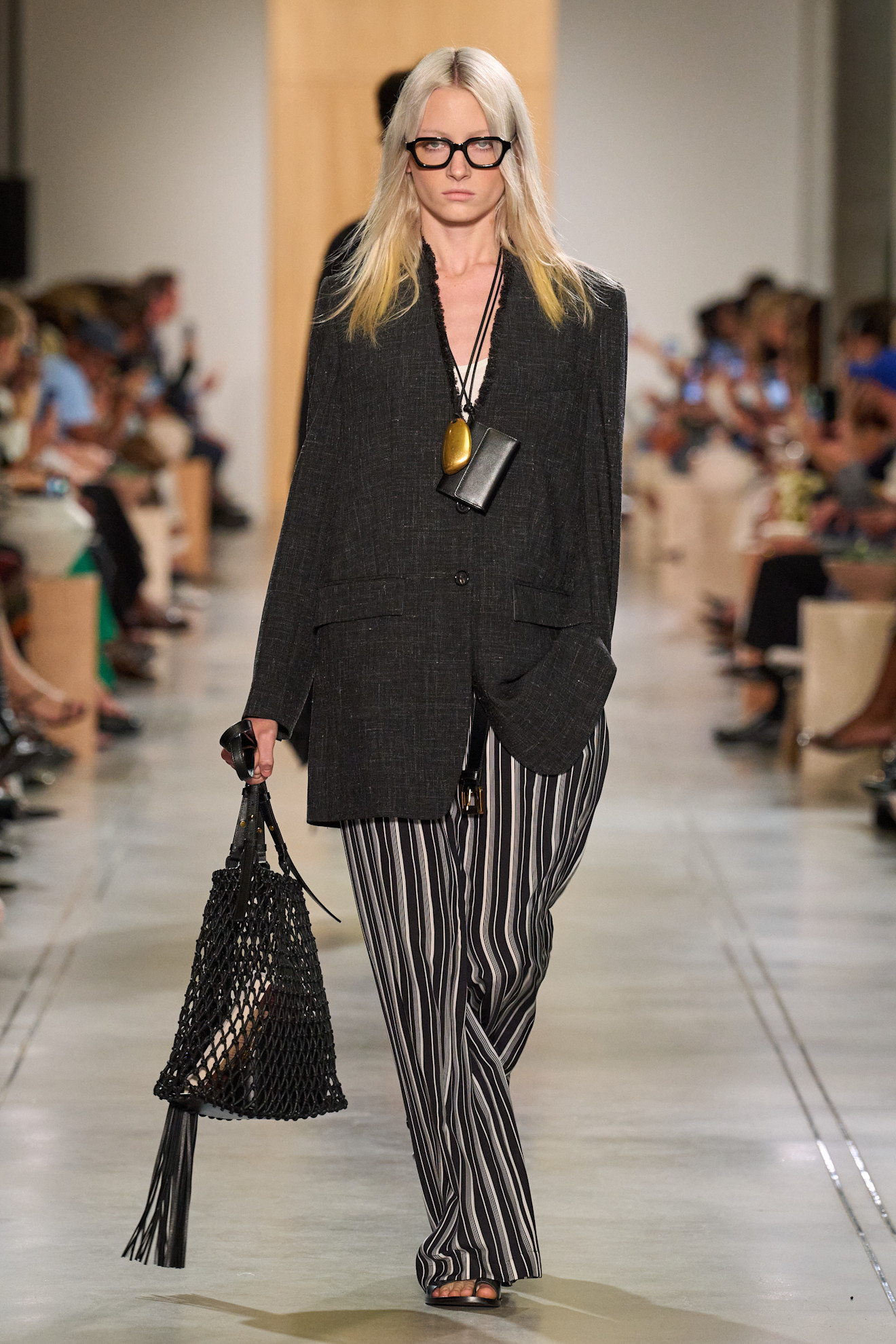 A Michael Kors model wearing a black collarless blazer and striped pants