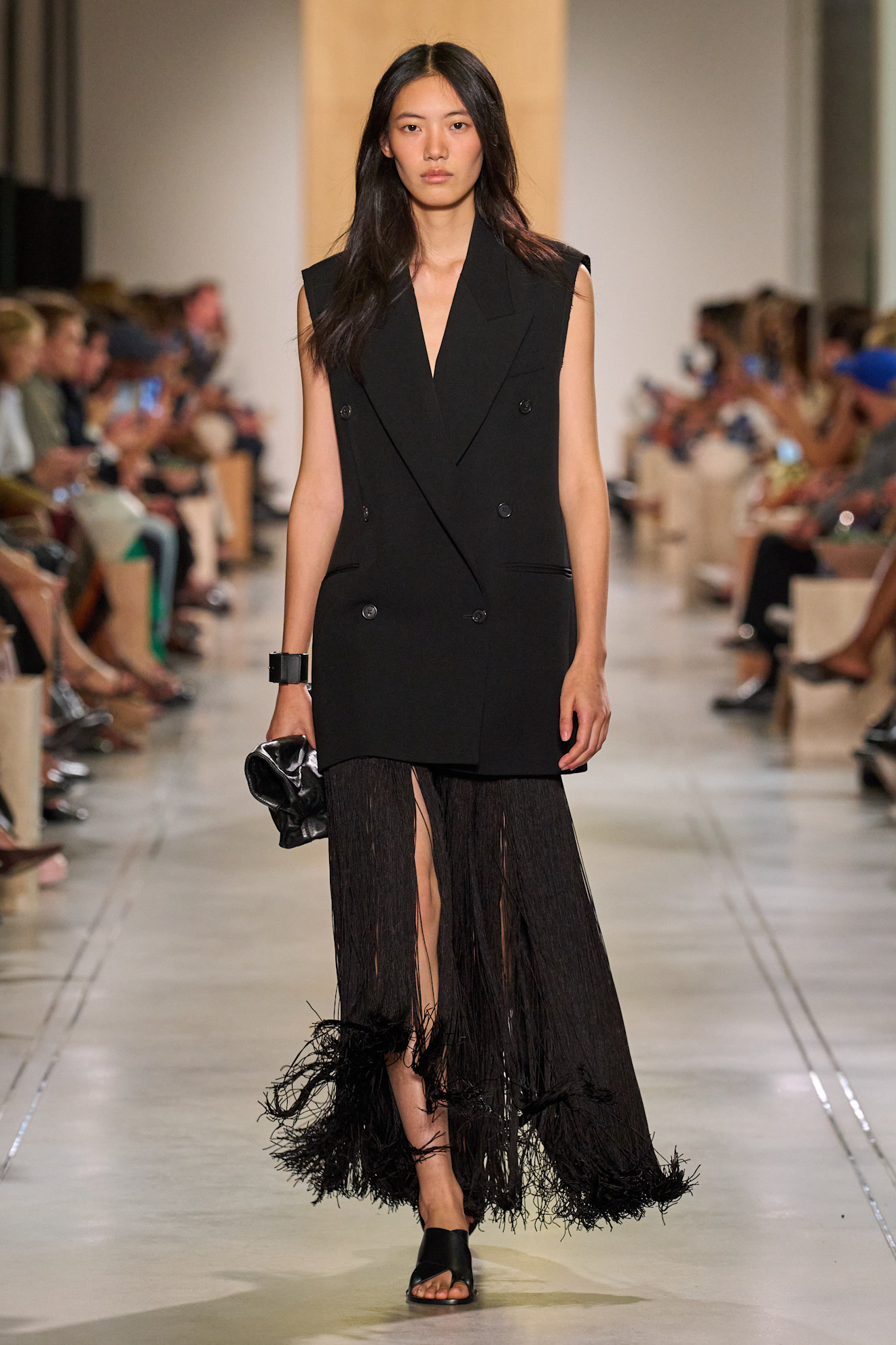 A Michael Kors model wearing a black sleeveless vest and a fringe skirt