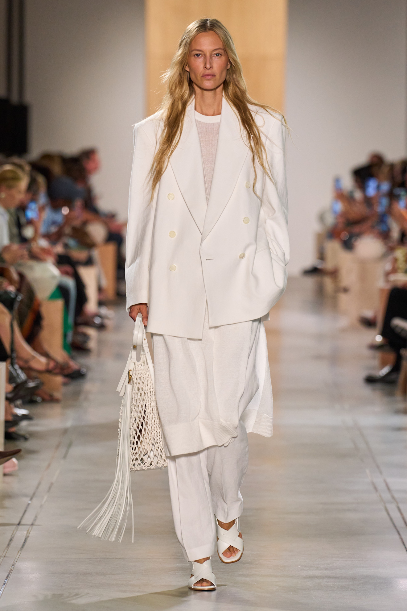 A Michael Kors model wearing a white oversized blazer, a sheer white tunic, and white pants
