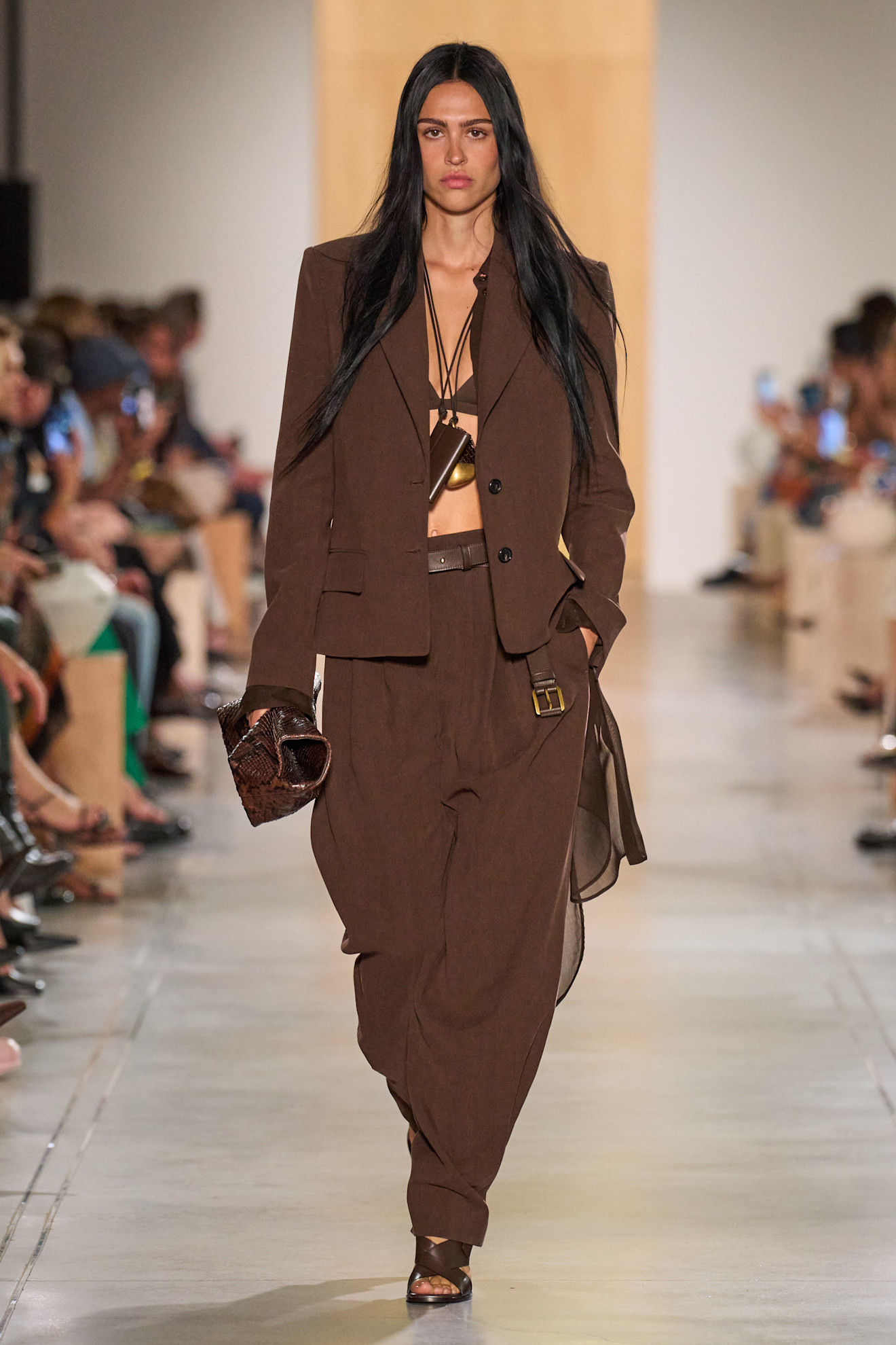 A Michael Kors model wearing a cropped brown blazer and brown tapered trousers