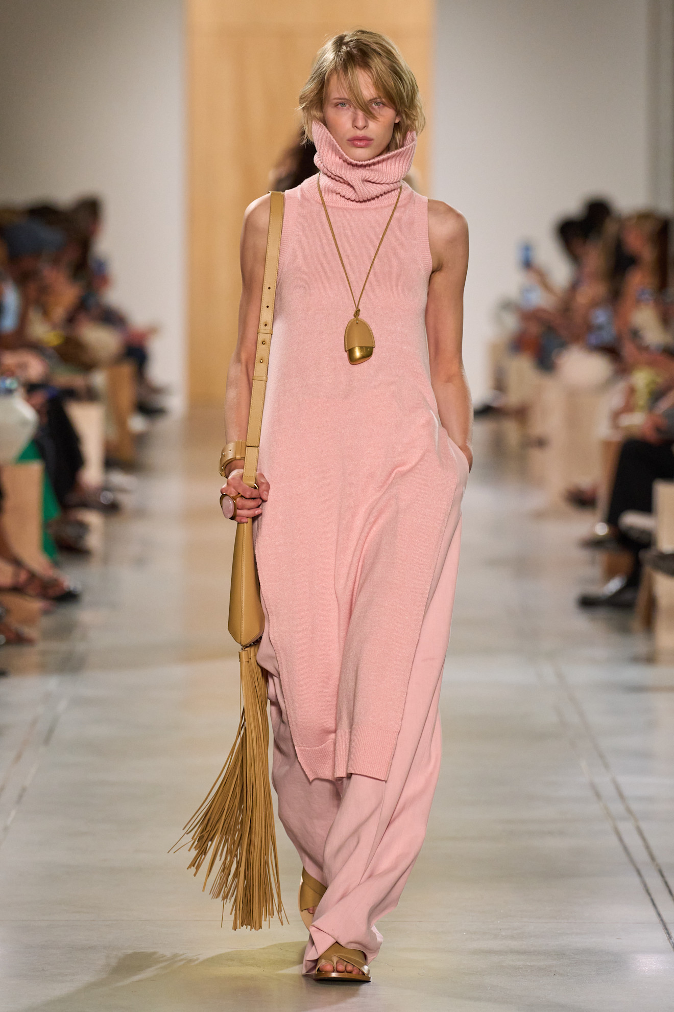 A Michael Kors model wearing a salmon knit tunic and pants, and a tan fringe shoulder bag
