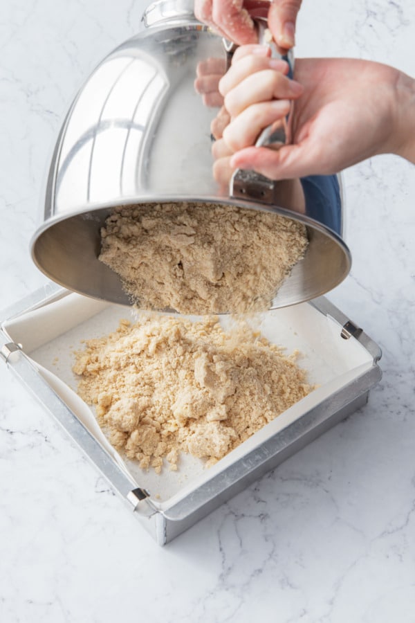 Pouring the shortbread cookie dough into a parchment-lined square baking pan.