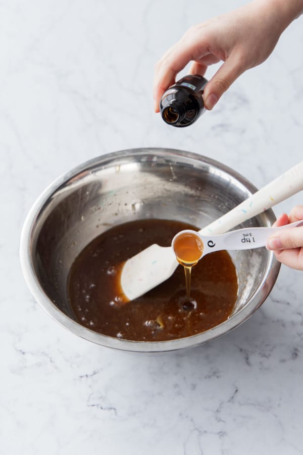 Adding vanilla and maple extracts to the mixing bowl.